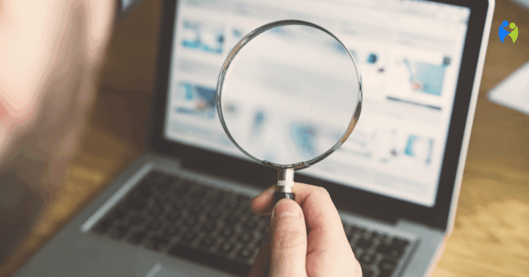Osoba trzyma lupę przed ekranem laptopa podczas wyszukiwania informacji w internecie – symboliczne przedstawienie autodiagnozy i cyberchondrii.