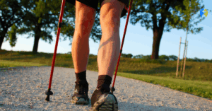 Osoba spacerująca z kijkami do nordic walking po żwirowej ścieżce w parku, widok na nogi i czerwone kijki, aktywność fizyczna na świeżym powietrzu.