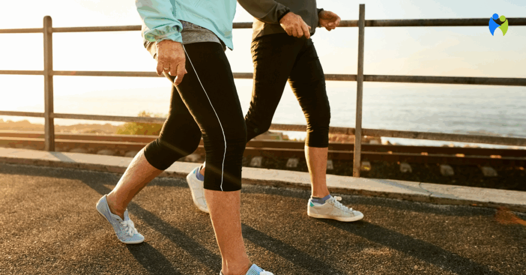 Dwie osoby w sportowych ubraniach spacerują wzdłuż nadmorskiej promenady o zachodzie słońca, dbając o kondycję i zdrowie stawów.