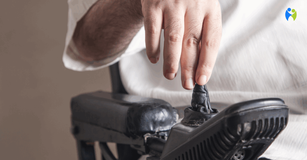 Zbliżenie dłoni mężczyzny obsługującego joystick wózka elektrycznego – sterowanie odbywa się za pomocą jednej ręki.