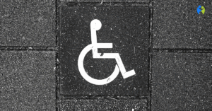 Symbol osoby na wózku inwalidzkim namalowany na czarnym chodniku z betonowych płyt.