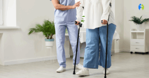 Fizjoterapeuta w stroju medycznym asekuruje i instruuje pacjentkę, która uczy się chodzić przy pomocy dwóch kul łokciowych w gabinecie rehabilitacyjnym.